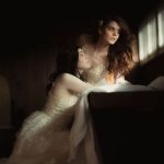 Gleichgeschlechtliches Paar in Spitzenkleidern, in einer dunklen Hütte mit Fenster, eine schaut nachdenklich zum Fensterlicht, die andere Blickt sie an