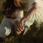 Ein Paar sitzt beieinander in einer Blumenwiese, schaut verträumt in die Umgebung, warmes Sonnenlicht scheint auf die beiden