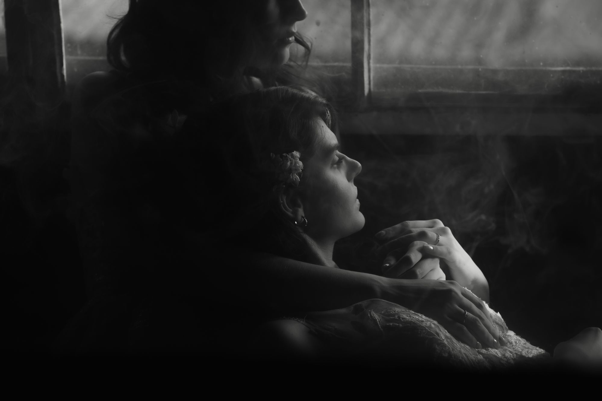 Schwarz Weiß Fotografie, Umarmung zweier Frauen, Berührungen der Hände und etwas Rauch rundherum