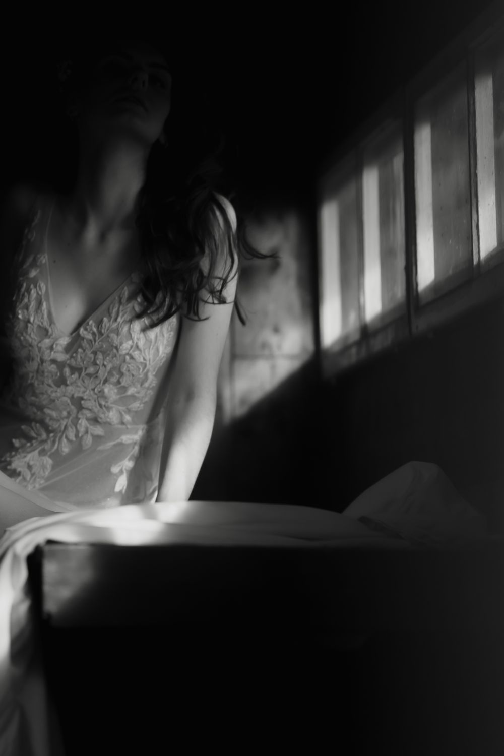 Verträumtes Hochzeitsportrait einer Braut in Schwarz Weiß, am Fenster sitzend