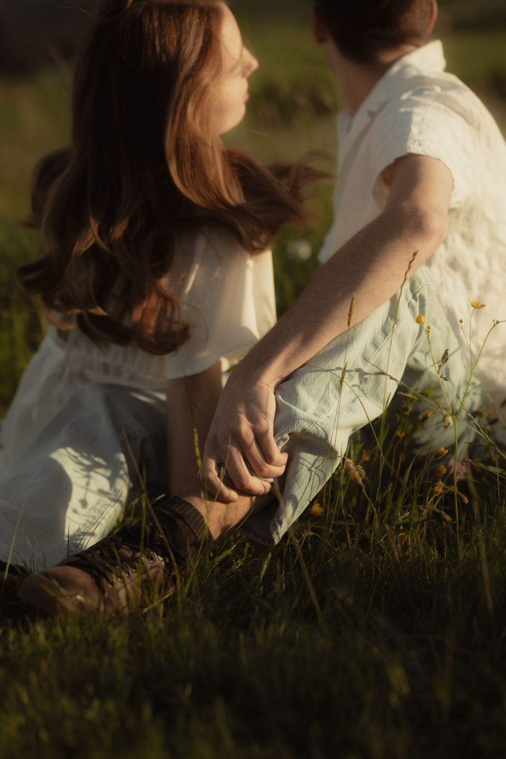 Ein Paar sitzt beieinander in einer Blumenwiese, schaut verträumt in die Umgebung, warmes Sonnenlicht scheint auf die beiden