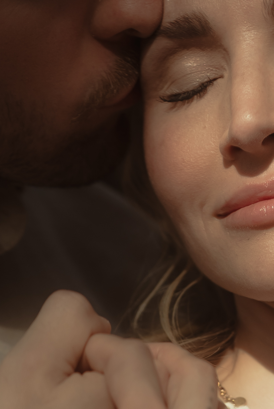 Sehr nahe, intime Aufnahme, auf der ein Mann sanft die Stirn der Frau kuesst, die ihre Augen geschlossen hat