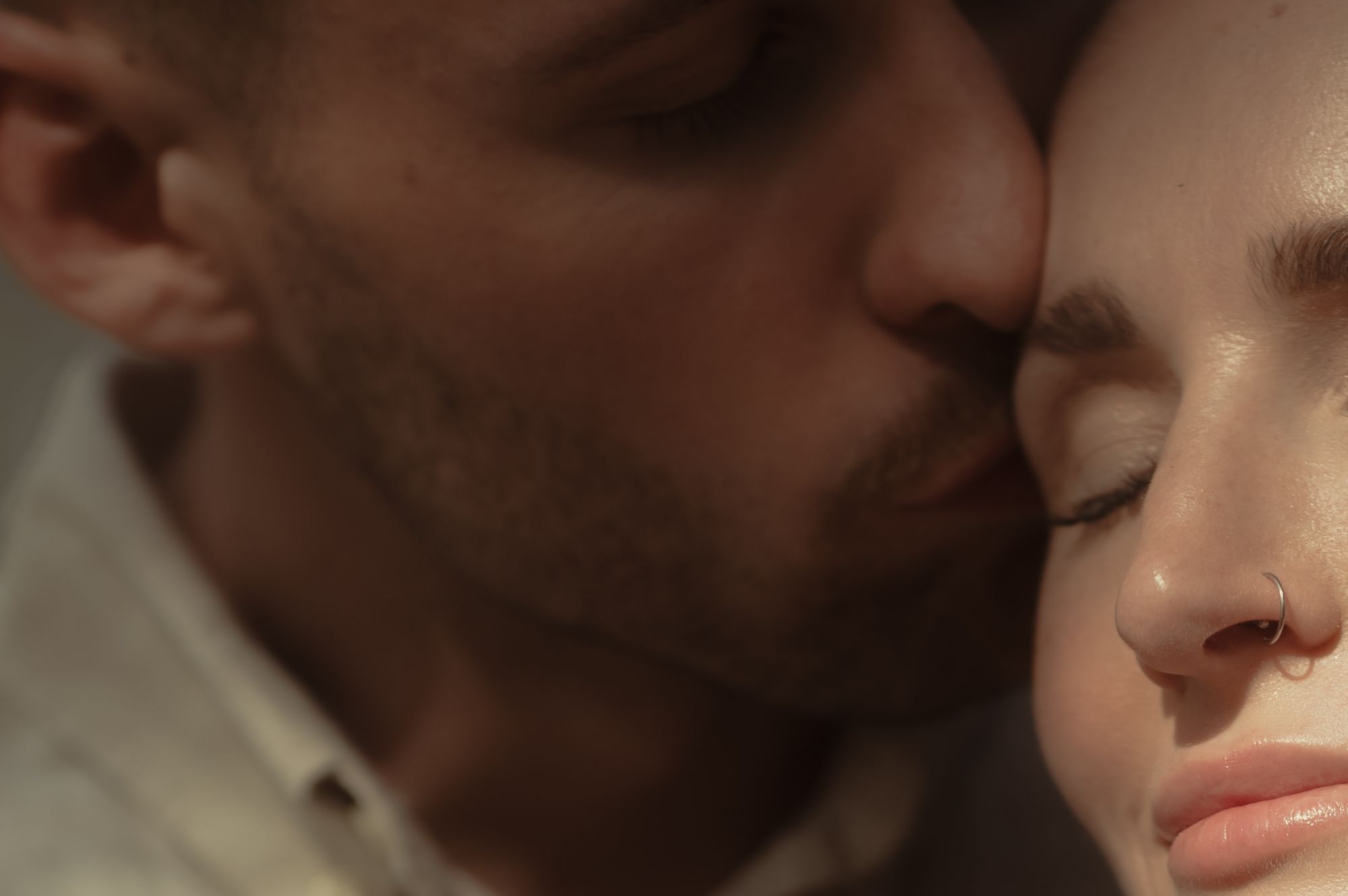 Nahaufnahme eines Paares, das die Gesichter aneinander schmiegt, er kuesst sie auf die Schlaefe, beide haben die Augen geschlossen